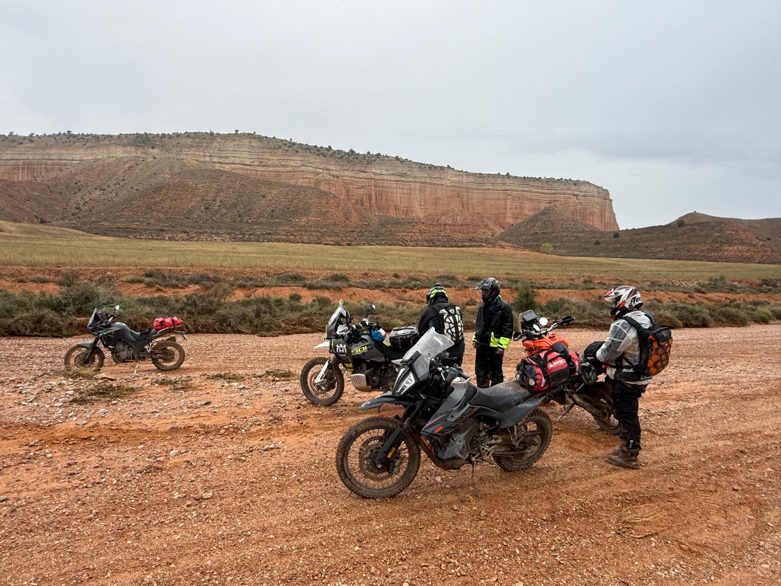 Cuatro motos trail y tres pilotos ante un plateau de arenisca en terreno desértico